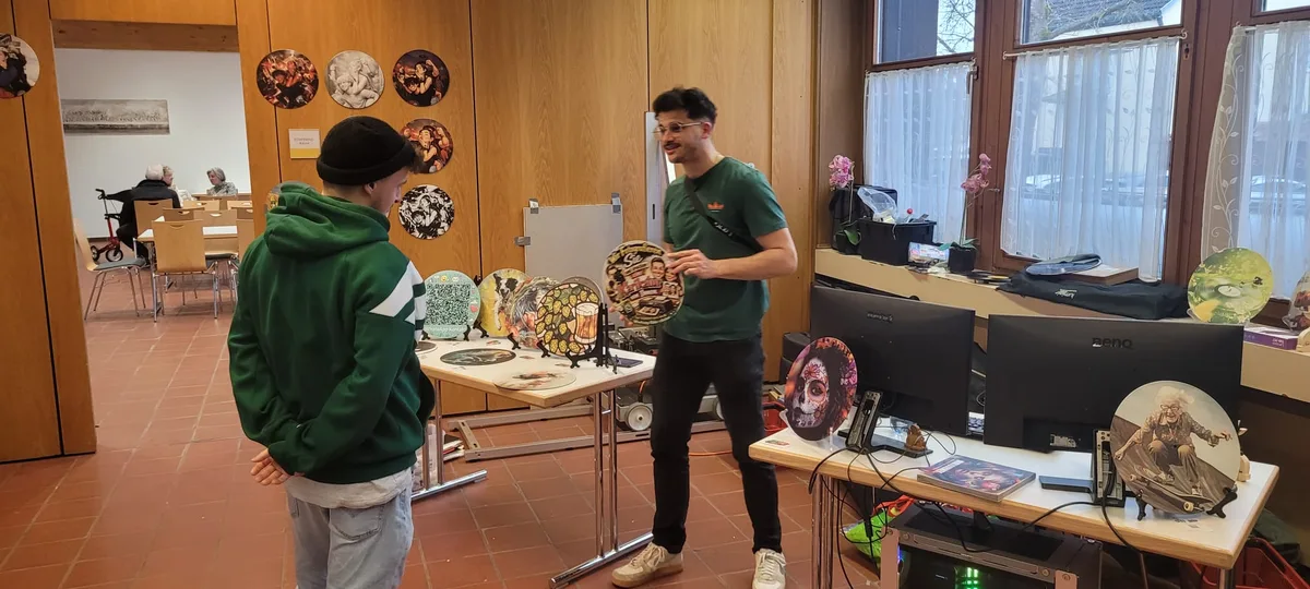 Sascha berät einen Besucher am Stand, dahinter viele Schallplatten